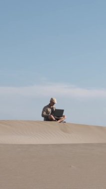 Adam çölde dizüstü bilgisayarla çalışıyor. Dijital göçebe ve uzaktan çalışan kavramı