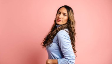 Kadın model ciddi ciddi kameraya bakıyor. Pembe arka planda yan poz veriyor.