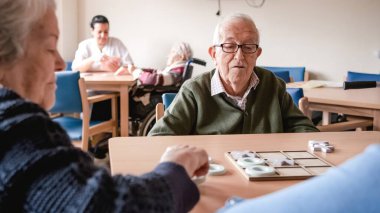 Son sınıf öğrencisi, huzur evinde birlikte vakit geçirirken masada arkadaşlarıyla Tic Tac Toots oynuyor.