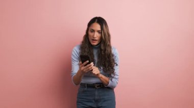 Pembe arka planda telefon kullanan bir kadın videosu ve aniden mutlu bir şekilde kutlama.