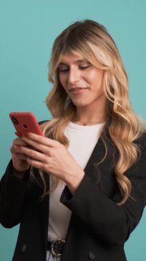 Akıllı gündelik kıyafetlerle mutlu transseksüel iş kadını mavi arka planda dururken akıllı telefondan mesaj atıyor.