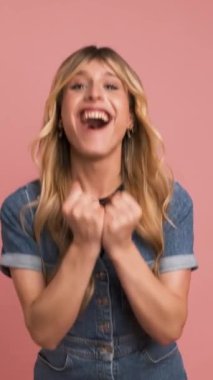 Heyecanlı transseksüel kadın, yumruklarını sıkarak bağırıyor zaferi kutlarken pembe arka planda duruyor.