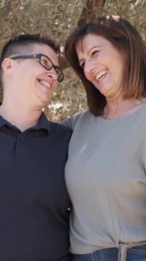 Zeytin ağacı tarlasında kucaklaşırken gülen mutlu lezbiyen çiftin yavaş çekim videosunu kapat.