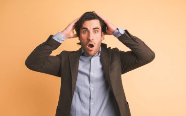 Blazer ceketli hayretler içinde bir iş adamının portresi. Kahverengi arka planda duran yüzünde şaşkınlık ve şaşkınlık ifadesiyle kameraya bakıyor.