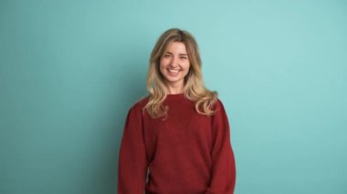 Kestane rengi kazaklı, uzun sarı saçlı, mavi arka planda gülen neşeli genç bayan.