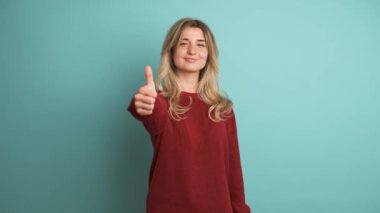 Mavi arka planda kameraya bakarken uzun sarı saçlı mutlu genç bir kadının portresi.