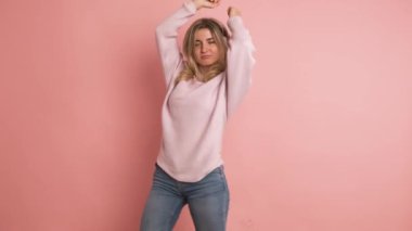Yavaş çekimde, pembe arka planda, kablosuz kulaklıklarla müzik dinleyen, dans eden, enerjik sarışın bir kadının videosu.