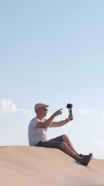 Adam kendini cep telefonuyla çöl kumullarında filme çekiyor. Seyahat eden erkek içerik yaratıcısı, etkili
