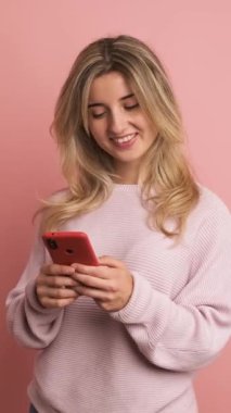 Stüdyo videosu ağır çekimde mutlu bir kadının pembe arka planında telefon duruşu ve gülümseme kullanarak