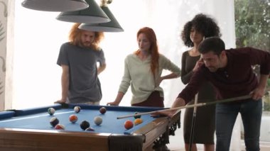 Çoklu etnik çeşitlilikteki erkek ve kadın arkadaşlar, hafta sonu evde oyun odasında bilardo sopasıyla bilardo oynayan genç adamı izliyorlar.