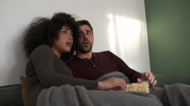 Hafta sonu evlerinde korku filmi seyrederken rahat koltukta mısır yiyen ürkek genç bir çift.