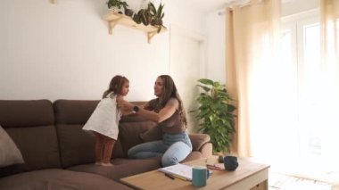 Gündüz vakti modern dairenin oturma odasında boş vaktini geçirirken küçük kızıyla rahat bir kanepede oynayan Latin anne yavaş hareket ediyor.