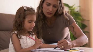 Hafta sonu evdeki oturma odasında keçeli kalemle kitap çizerken kanepeye oturan mutlu Latin anne ve tatlı kızın yavaş çekimleri.