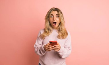 Stüdyo videosu ağır çekimde pembe arka planda telefon kullanan bir kadının şaşırtıcı yeni bir telefon alışı.