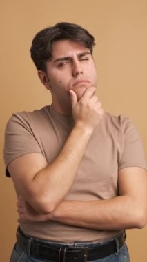 Stüdyoda kahverengi arka planı olan düşünceli bir yüz ifadesiyle el ele tutuşan şüpheli bir adam.