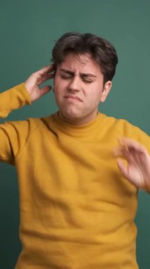 Sarı kıyafetli düşünceli genç bir erkek, yeşil arka planda baş ağrısından muzdarip.