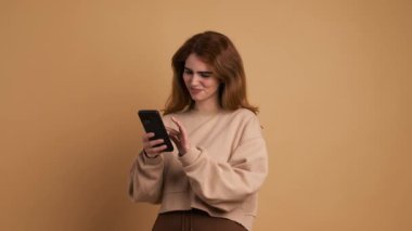 Telefon kullanan ve gülümseyen genç bir kadının kahverengi geçmişine sahip bir stüdyo videosu.