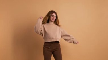 Kameraya doğru mutlu bir şekilde dans eden genç bir kadının kahverengi arka planlı stüdyo videosu.