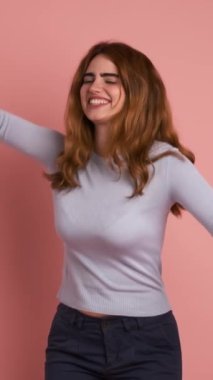 Pembe arka planı olan bir stüdyo videosu genç bir kadının kollarını kaldırmasını kutluyor. Dikey Görüntü