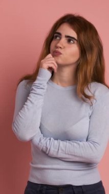Düşünceli bir kadının elleri çenesinde pembe arka planı olan bir stüdyo videosu. Dikey Görüntü