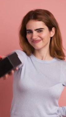 Mutlu bir kadının hediye verip gülümsediği pembe arkaplanlı bir stüdyo videosu. Dikey Görüntü