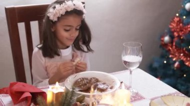 Beyaz giyinmiş bir kızın Noel yemeğinde dikkati dağılmış bir şekilde yemek yerken videosu.