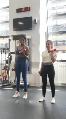 Modern spor salonundaki dambılları kullanarak beden eğitimi dersi veren bir eğitmenin yavaş çekim videosu.