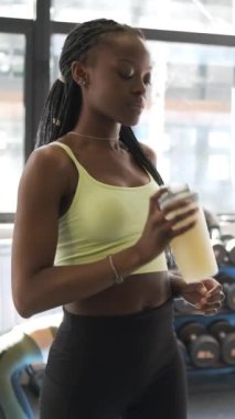 Sporcu bir kadın spor salonunda antrenman yaparken protein içeceğini karıştırıyor. Spor, sağlıklı ve aktif yaşam konsepti.