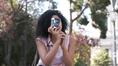 Siyah kıvırcık saçlı Afro-Amerikalı kadın güneşli bir günde dijital kamera kullanarak şehir parkında fotoğraf çekiyor.
