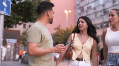 Gündelik giysiler içindeki İspanyol kadınlar, şehir caddesinde akıllı telefon kullanan bir adamdan yardım istiyorlar.