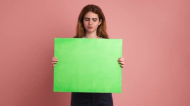 Yeşil paneli tutan endişeli ve üzgün genç bir kadının pembe arkaplanlı videosu.