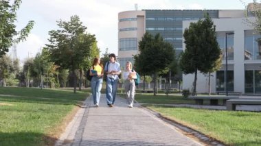 Güneşli bir günde, üniversitenin kampüs yolunda yürürken gündelik kıyafetleriyle sohbet eden bir sürü genç adam.