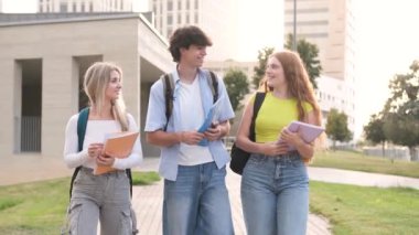 Üniversite kampüsünde yürürken ve sohbet ederken günlük giysiler içinde gülümseyen genç erkek ve bayan öğrencilerin ağır çekimde