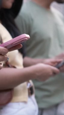 Şehirde kaldırımda dikilirken akıllı telefonlar kullanan gündelik kıyafet giymiş isimsiz erkek ve kadın arkadaşlarının orta kesimi.