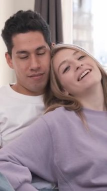 Genç, çok ırklı bir çift evdeki rahat bir kanepede sarılıp birbirlerine eşlik ederek mutlu anlarını paylaşıyorlar.