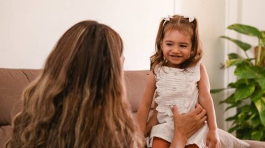 Eğlenceli Latin anne, haftasonunu evde birlikte geçirirken küçük kızını kanepede gıdıklıyor.