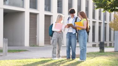Güneşli bir günde üniversite kampüsünde masa kullanan, kitap ve sırt çantalı, sıradan giyinmiş, mutlu genç erkek ve kız öğrencilerden oluşan bir vücut.