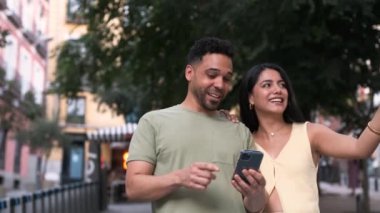 Gündüz vakti şehir sokaklarında yürürken akıllı telefonları birlikte kullanırken gündelik giysiler içinde neşeli, genç İspanyol bir çift onları işaret ediyor.