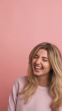 Pembe arka planda bir stüdyo videosu. Kafkasyalı genç bir kadın enerjik bir şekilde gülüyor.