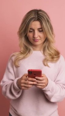 Stüdyo videosu ağır çekimde pembe arka planda telefon kullanan bir kadının şaşırtıcı yeni bir telefon alışı.