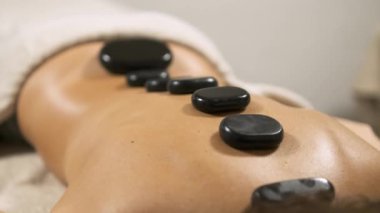 Müşteri masaj masasında yatıyor ve masaj terapistinden sıcak taş masajı alıyor.