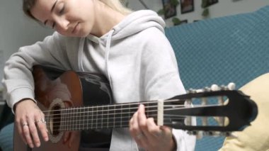 Genç bir kadın akustik bir gitarın tellerini koparıyor, rahat bir ortamda rahatlatıcı bir melodi yaratıyor.