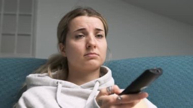 Bir kadın kanepeye oturup uzaktan kumandayla kanal değiştirip ilgi çekici bir şey ararken can sıkıntısı başlıyor.