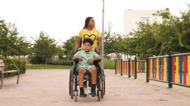 Kardeşinin arkasından yürüyen bir kadın, parkta tekerlekli sandalyeyi iterken onunla sıcak bir şekilde konuşuyor. Sahne, barışçıl ve doğal ortamda onların yakın bağlarını yakalıyor.