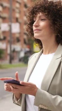 İş kadını akıllı telefonuyla şehir caddesinde iletişim kuruyor modern teknoloji ve şehir yaşam tarzını sergiliyor. Dikey görüntüler