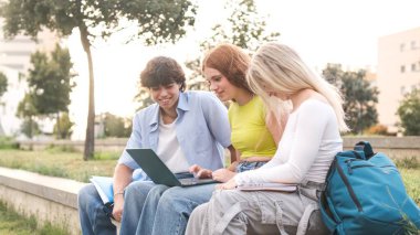 Gündelik elbiseli genç bir kadın üniversite kampüsünde sınıf projesi üzerinde çalışırken dizüstü bilgisayar kullanıyor.