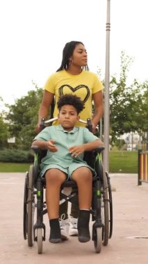 Anne oğlunu tekerlekli sandalyeyle güneşli bir parka itiyor. Doğanın tadını çıkarırken içten bir sohbete dalıyor. Dikey görüntüler