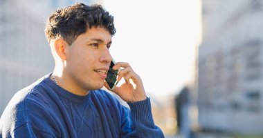 Şehirde güneşli bir günün tadını çıkarırken akıllı bir telefonla sohbet eden genç adam rahat ve neşeli bir şehir yaşam tarzını somutlaştırıyor.