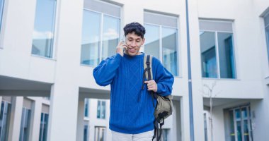Genç Latin üniversite öğrencisi bir üniversite kampüsünde yürürken akıllı telefon kullanıyor, dışarıda iletişim ve bağlantının keyfini çıkarıyor.