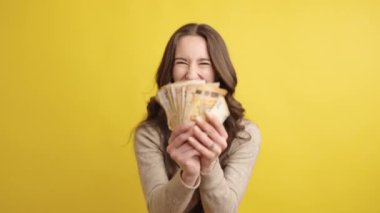 Neşeli bir kadın, avroluk banknotların hayranını enerjik bir şekilde tutuyor ve sergiliyor. Parlak sarı bir arka planda mutluluk ve başarı yayıyor.